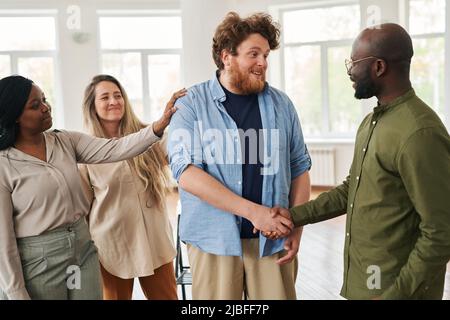 Deux jeunes hommes interraciaux heureux qui se secouent la main avant ou après une session psychologique tout en se tenant contre des femmes gaies Banque D'Images