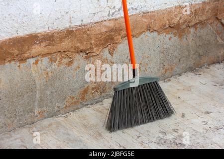 Un grand balai de nettoyage de rue se tient contre un mur de béton sur l'asphalte Banque D'Images