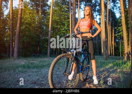Posez la femme avec un vélo dans la forêt Banque D'Images