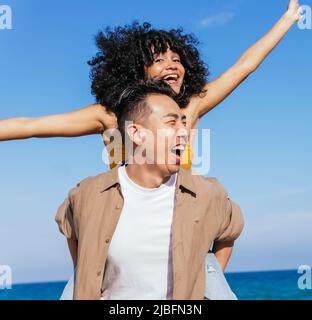 Gai asiatique copain dans des vêtements décontractés prendre petite amie dans le pigegyback contre la mer et le ciel bleu Banque D'Images