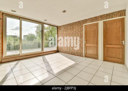 Intérieur d'une chambre vide spacieuse avec sol carrelé avec portes en bois près du mur de briques et portes en verre menant au balcon Banque D'Images