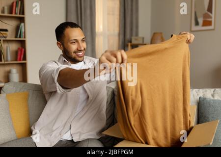 Jeune homme noir unboxing carton paquet, heureux de shopping réussi, satisfait avec grand achat à la maison Banque D'Images