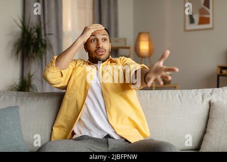 Jeune homme noir émotif exprimant son indignation, choqué par les mauvaises nouvelles ou la défaite de l'équipe sportive à la télévision à la maison Banque D'Images