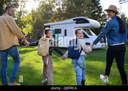 Une vue arrière de la jeune famille avec des valises allant à la caravane à l'extérieur au parc. Banque D'Images