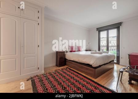 Chambre double avec belle décoration en bois noble, placards blancs, tapis et balcon avec portes en verre et aluminium de couleur bronze Banque D'Images