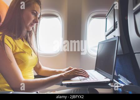 Femme utilisant un ordinateur portable pendant qu'elle est assise dans un avion près de la fenêtre Banque D'Images