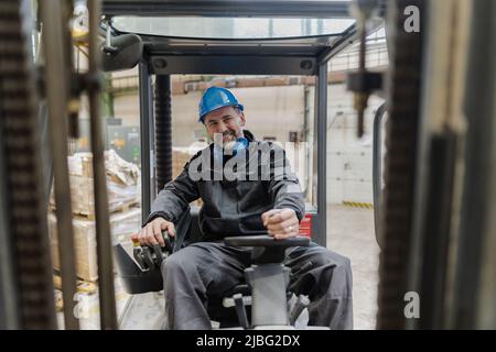 Homme mûr heureux chariot élévateur conducteur de levage de la palette dans l'entrepôt de stockage et regardant la caméra. Banque D'Images