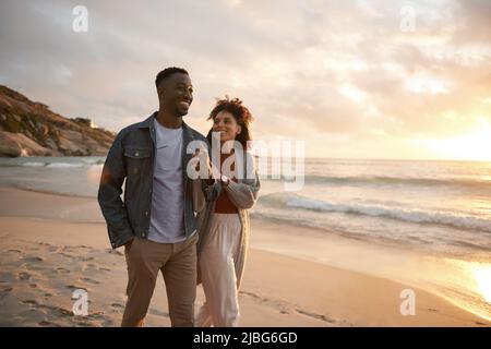 Jeune couple multiethnique souriant marchant le long d'une plage au coucher du soleil Banque D'Images