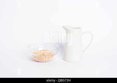 Carafe de lait d'avoine non laitier et flocons d'avoine dans un bol en verre sur fond blanc. Concept alimentaire végétalien sain. Banque D'Images