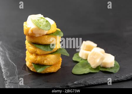 Porridge italien frit sous forme de crêpes polenta sur fond noir avec fromage macarella et épinards Banque D'Images