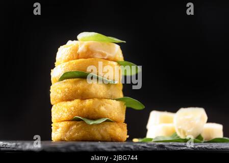 Porridge italien frit sous forme de crêpes polenta sur fond noir avec fromage macarella et épinards Banque D'Images