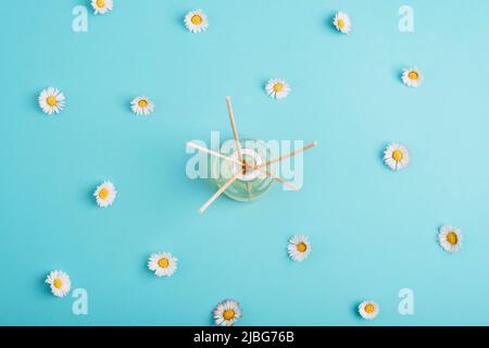 Bouteille en verre de diffuseur d'arôme et fleurs de Marguerite sur fond bleu clair. Concept d'été. Vue de dessus, plan d'appartement. Banque D'Images