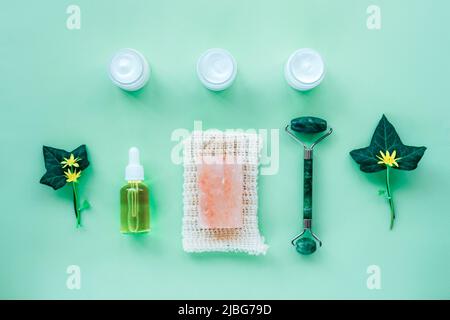 Beauté cosmétique rouleau facial, bocaux de crème, flacon compte-gouttes de sérum et savon sur fond vert, vue de dessus, plat. Concept de produits naturels pour la peau Banque D'Images