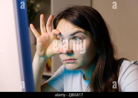 La femme se force à regarder dans l'écran de l'ordinateur, en ouvrant ses yeux larges avec ses mains Banque D'Images