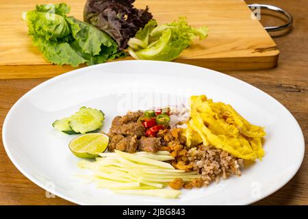 Gros plan de la pâte de crevettes riz frit avec crevettes sèches croustillantes, porc doux, omelette, morceaux de mangue brute hachée, demi citron, morceaux de concombre, piec Banque D'Images