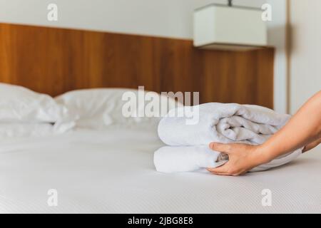 Mains mettant des serviettes de bain blanches fraîches sur le drap de lit. Banque D'Images