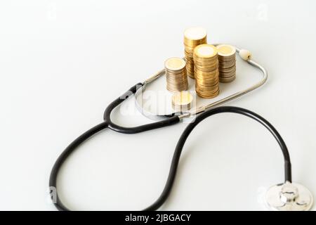 Photo de gros plan du stéthoscope et des pièces empilées sur un arrière-plan isolé. Concept de la hausse des coûts des dépenses de santé. Banque D'Images