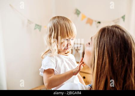 Un petit enfant regarde et touche le visage de sa mère. Maman enseigne à la petite fille de prendre soin de la peau du visage Banque D'Images