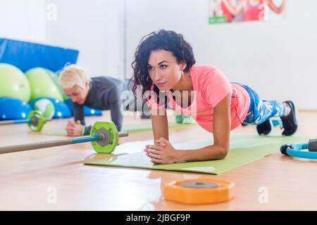 Jeunes filles sportives attrayantes faisant de l'exercice de planking d'avant-bras de yoga ou pose de dauphin sur des tapis pendant l'entraînement dans le club de fitness. Banque D'Images