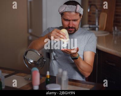 Concept de beauté pour hommes. Un homme de race blanche qui vérifie sa peau. Un homme à la barbe tire la crème de soin de la peau, la main des hommes en utilisant de la crème hydratante, la peau et la main Banque D'Images