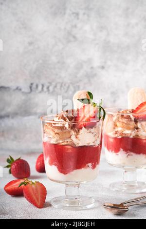 Tiramisu fraise. Dessert italien traditionnel tiramisu en verre avec feuilles de fraise et de menthe fraîches sur fond de table rétro en béton gris Banque D'Images