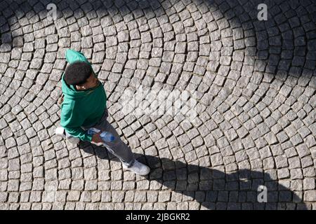 Un homme noir non identifié portant un chandail vert et une bouteille d'eau de source marche à la main le long d'une rue pavée de Maastricht. Vue d'en haut, longue chiade Banque D'Images