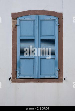 Les volets courbés peints en bleu avec grilles au sommet sont suspendus avec des charnières en métal dans un cadre en pierre rouge dans un mur en plâtre gris Banque D'Images