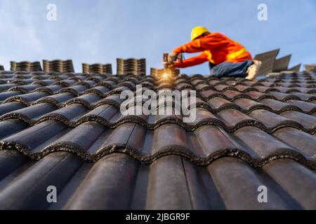 Un ouvrier de la construction installe un nouveau toit, perceuse électrique utilisée sur les nouveaux toits avec tuiles de toit en béton, outils de toiture. Mise au point sélective de toit en béton jusqu'au Banque D'Images