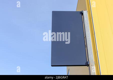 Affiche vierge noire avec pôle installé à côté du bâtiment jaune par beau temps. Le pôle est rouillé. Banque D'Images