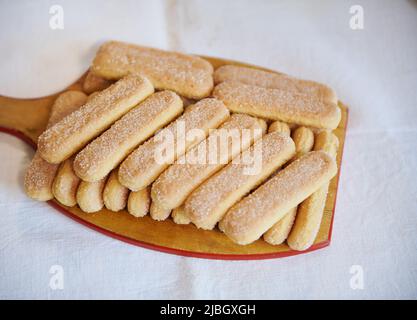 Vue depuis le dessus des biscuits savoiardi de ladyfinger sur une planche à découper en bois sur fond de nappe blanche. Gros plan Banque D'Images