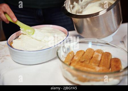 Gros plan. Le chef met à la main un mélange de mascarpone et de crème fouettée sur le gâteau tout en faisant du tiramisu - dessert italien traditionnel à la maison. Banque D'Images