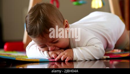 Bébé contrarié pleurant, fatigué en colère un enfant d'un an allongé sur un tapis de jeu ayant une colère Banque D'Images