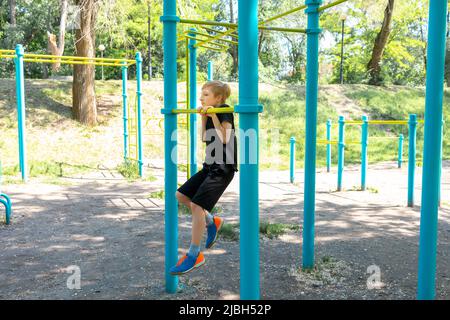 un garçon sportif dans la rue du parc effectue des pull-ups sur la barre transversale Banque D'Images