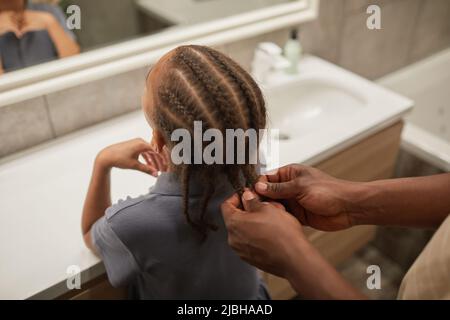 Gros plan sur les soins de père noir tressant les cheveux des filles dans la salle de bains et aidant à se préparer le matin Banque D'Images