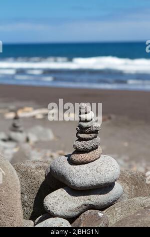 Petit cairn de rochers de lave arrondis sur une plage hawaïenne avec l'océan Pacifique en arrière-plan. Banque D'Images