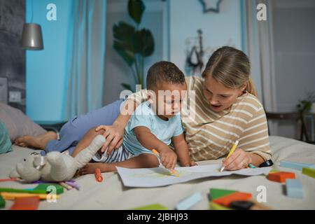 Portrait d'une mère caucasienne heureuse avec un joli dessin de bébé de race mixte allongé sur le lit Banque D'Images