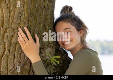 Une jeune femme contentée embrasse un grand arbre avec une expression blissful et ses yeux fermés dans un concept de sauver la forêt, d'arrêter la déforestation, le jour de la terre, en lien avec la nature et la conservation de la nature. Photo de haute qualité Banque D'Images