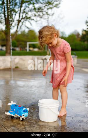 Petite fille jouant avec des jouets au terrain de jeux de la zone d'eau dans le parc en été. Un petit enfant près des fontaines passe du temps à l'extérieur Banque D'Images