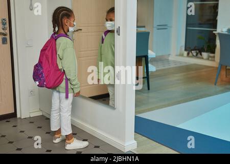 Vue latérale portrait d'une fille afro-américaine portant un masque et un sac à dos pour retourner à l'école en septembre, espace copie Banque D'Images