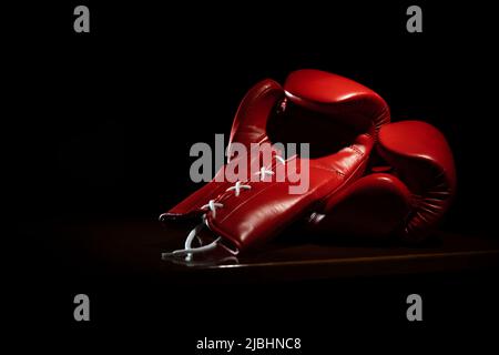 Nouveaux gants de boxe rouge brillants avec lacets dans un éclairage tamisé sur fond noir Banque D'Images