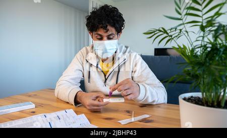 Homme portant un masque plaçant l'échantillon dans un compte-gouttes tampon pour la détection du coronavirus à la maison. Test PCR après retour de la foule et rencontre p Banque D'Images