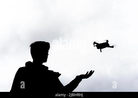 Silhouette d'un jeune homme volant un drone à l'extérieur avec le ciel en arrière-plan Banque D'Images