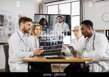 Groupe de chercheurs médicaux multiethniques ayant un séminaire en ligne vidéo à distance avec des collègues professionnels dans la salle de conférence de laboratoire. Les scientifiques parlent des résultats de la tomographie pour le développement efficace. Banque D'Images