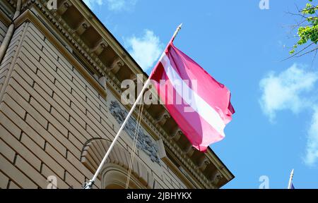 Le symbole officiel de la Lettonie est un drapeau avec deux rouges et entre la bande blanche contre un ciel bleu qui flotte dans le vent Banque D'Images