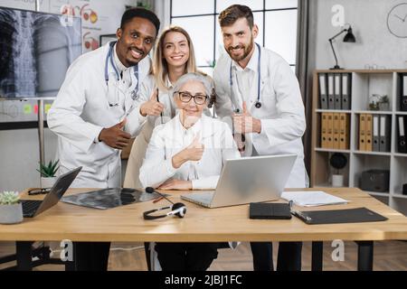 Des chercheurs heureux se posant sur la caméra avec le sourire devant l'ordinateur portable tout en travaillant sur un nouveau projet scientifique. Le personnel de laboratoire multiethnique qui fait des découvertes médicales dans une société pharmaceutique moderne se départir Banque D'Images