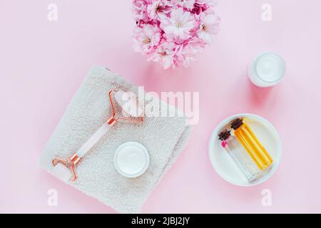 Ensemble de cosmétiques naturels bio spa avec fleurs de sakura. Rouleau de visage, crème cosmétique, serviette et huile sur fond rose. Soins de la peau, soins de beauté co Banque D'Images