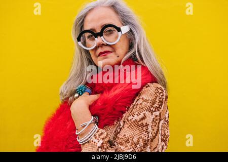 Femme âgée regardant la caméra tout en se tenant contre un fond de citron. Femme âgée élégante, pleine de confiance et de jeunesse, vêtue d'un rouge Banque D'Images