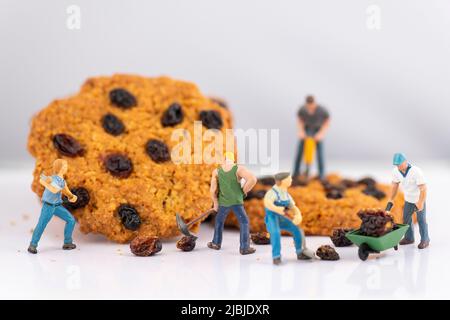 Personnes miniatures, petit modèle de figure humaine enlever les raisins secs des biscuits Banque D'Images