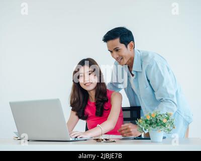 Joyeux couple asiatique, jeune femme et homme utilisant une tablette et un ordinateur portable ensemble pour la réservation de vol, la chambre d'hôtel et les informations de voyage à la maison, prêt t Banque D'Images