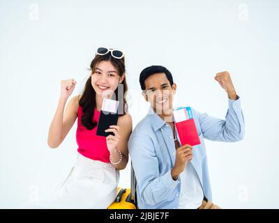 Prêt à voyager, joyeuses vacances. Concept de vacances d'été. Un couple asiatique souriant tenant le poing levé, montrant passeport avec succès, jeune femme et homme Banque D'Images